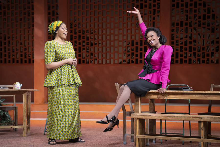 Photo from the Goodman production of "School Girls; Or, the African Mean Girls Play," featuring two women in colorful costumes in a schoolroom setting, Tania Richard and Lanise Antoine Shelley
