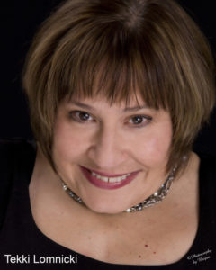 Close shot of woman with brown hair cut in a bob style, wearing a black top and a glittery necklace.
