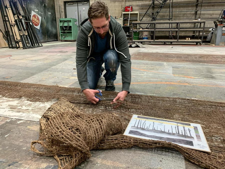 Designer in a studio scissors through some burlap material for a scenic element.