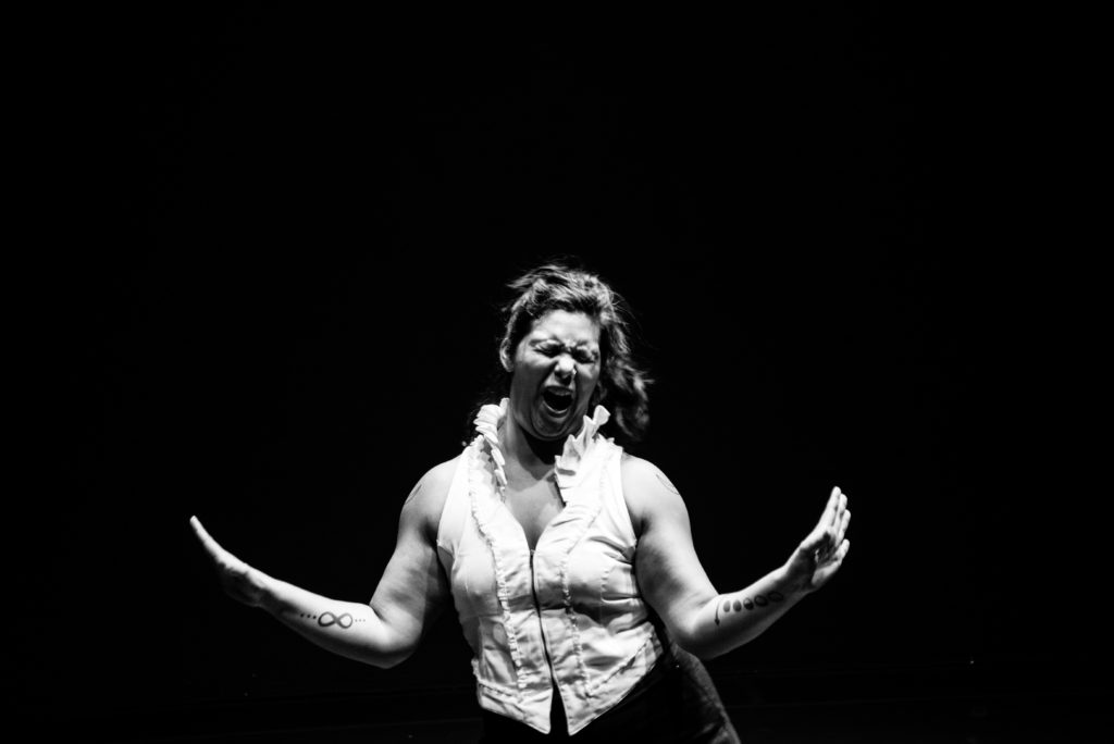 Dancer in a black-and-white image, starkly lit, gestures fiercely, mouth open, eyes closed.